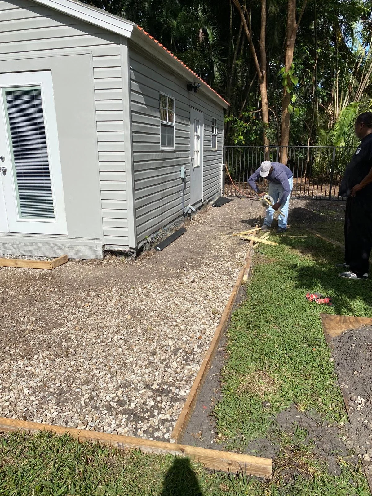 Prepared ground and timber forms beside a small building during Belou Stucco project work