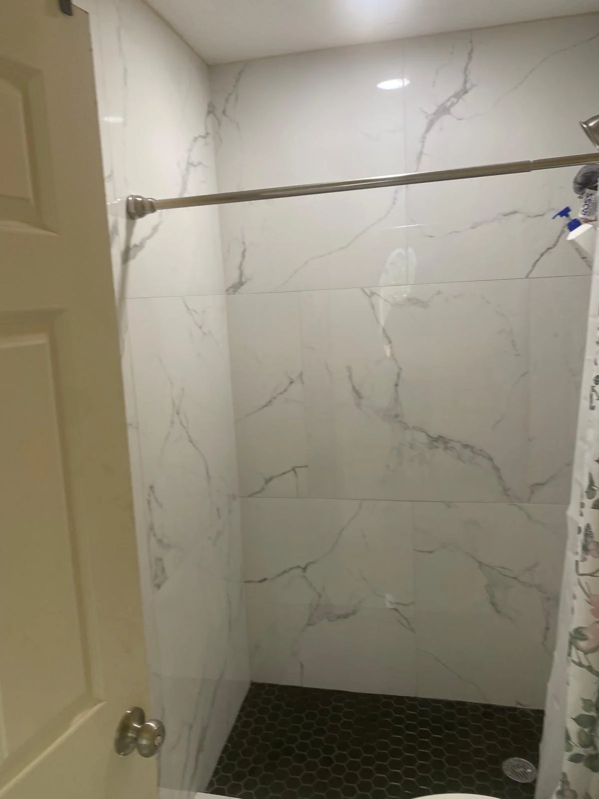 Marble-look shower wall tile above a dark hexagonal tile floor